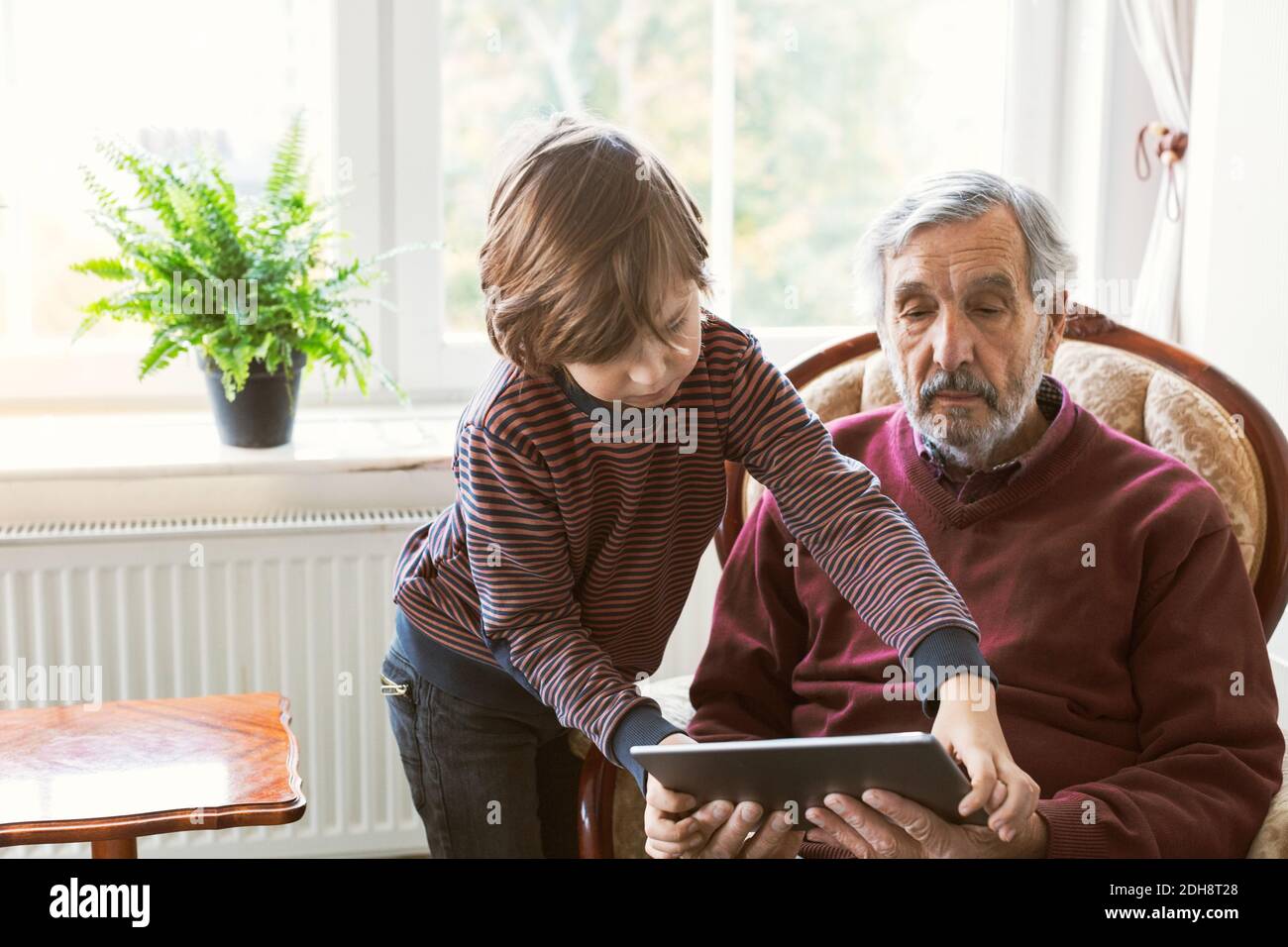 Ragazzo che assiste il nonno nell'uso del tablet digitale a casa Foto Stock