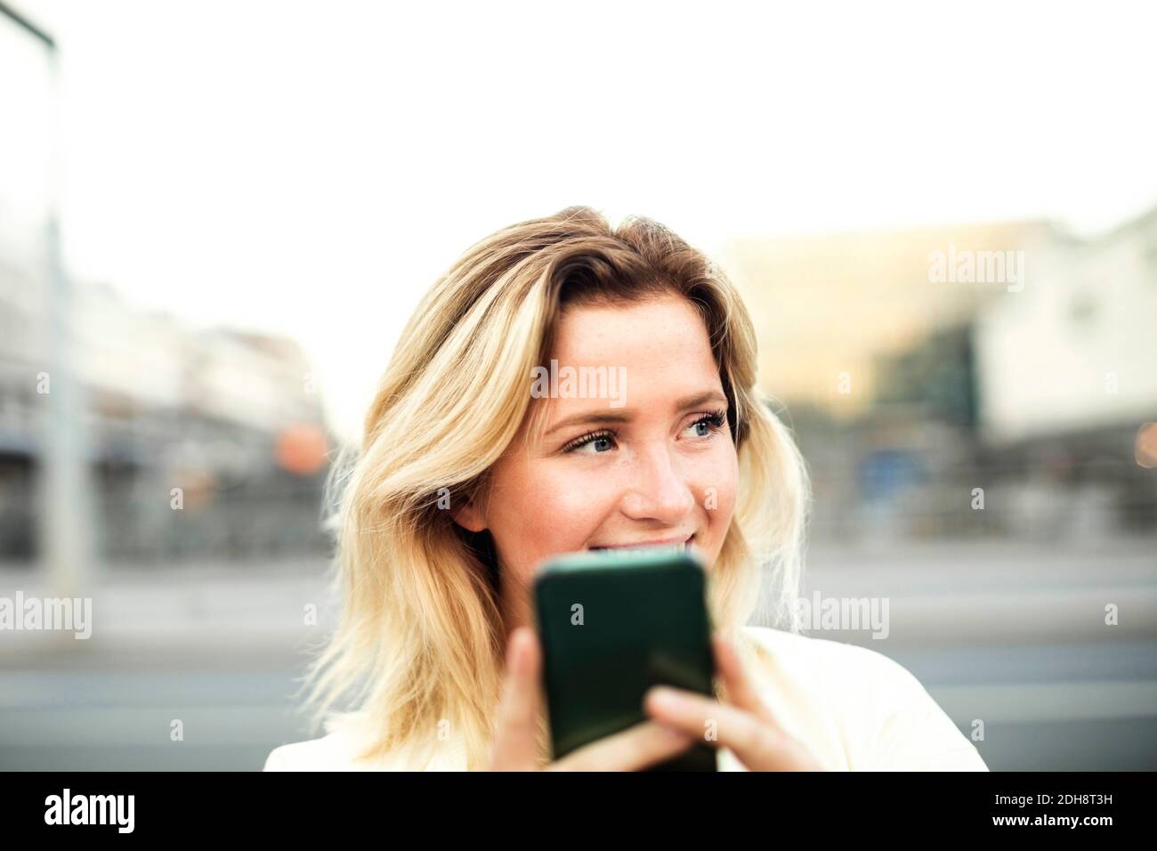 Felice giovane donna che usa il telefono cellulare in città contro chiaro cielo Foto Stock