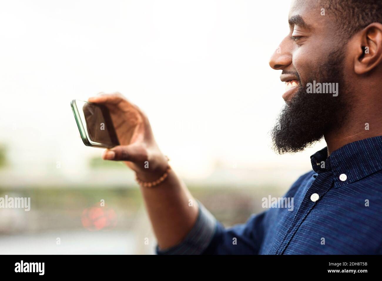 Vista laterale di un giovane uomo che fotografa dal telefono cellulare contro cielo Foto Stock