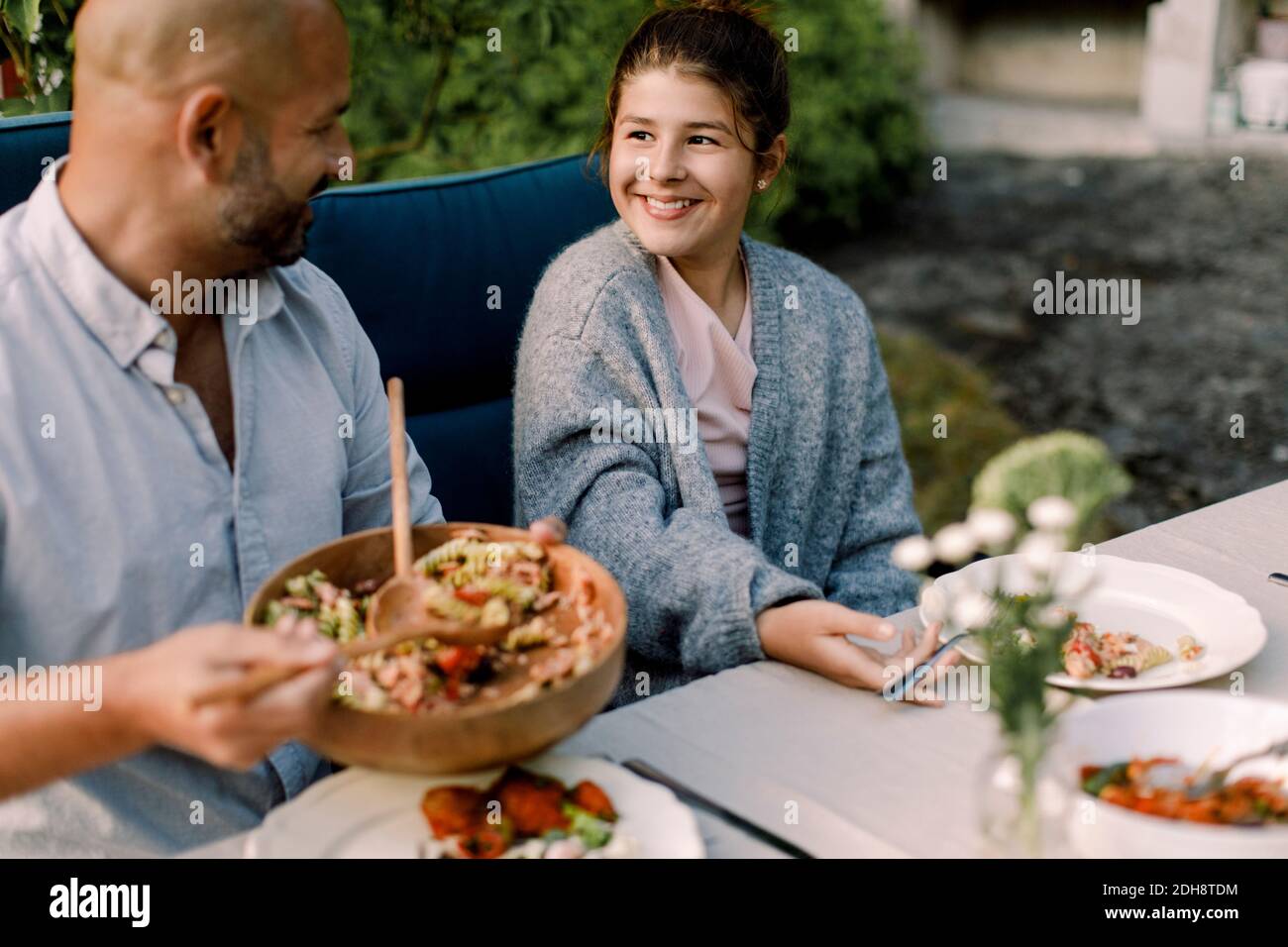 Padre che guarda sorridere figlia mentre serve cibo a cena tavolo in cortile Foto Stock