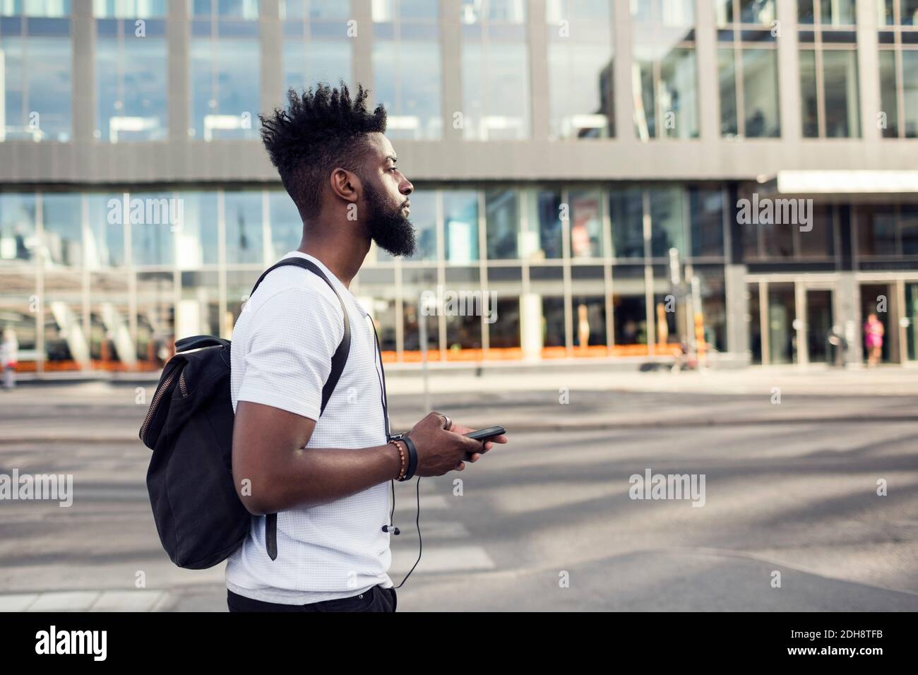 Vista laterale di un giovane che tiene in mano uno smartphone mentre si è all'interno città Foto Stock