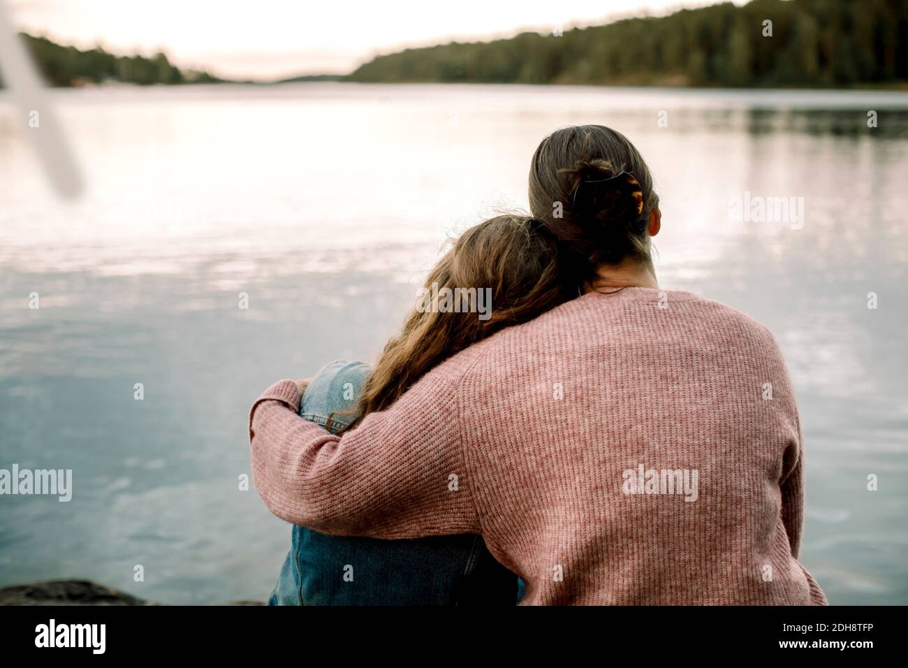 Vista posteriore di madre con figlia seduta sul lago Foto Stock