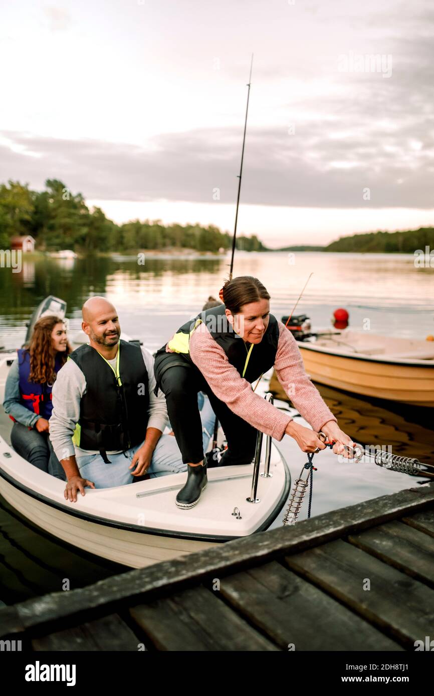 La famiglia guarda la donna ancorando la barca sul molo durante il tramonto Foto Stock