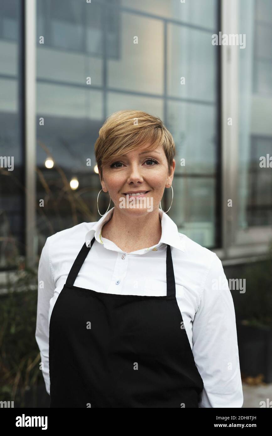 Ritratto di un grembiule sorridente e professionale in piedi contro un edificio in vetro Foto Stock