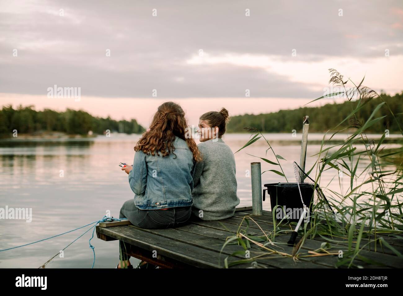 Sorridente ragazza che parla con il fratello mentre si siede sul molo durante tramonto Foto Stock