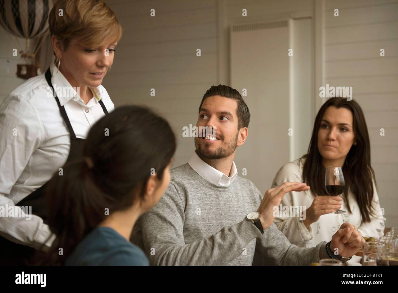 La gente di affari che parla con la donna che indossa il grembiule mentre winetasting a. tabella Foto Stock