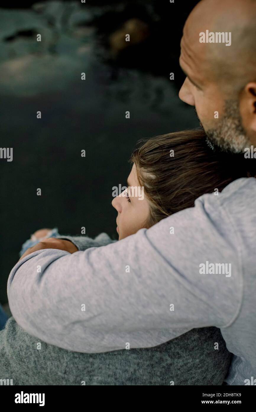 Padre e figlia che guardano via mentre si siedono sul lago Foto Stock