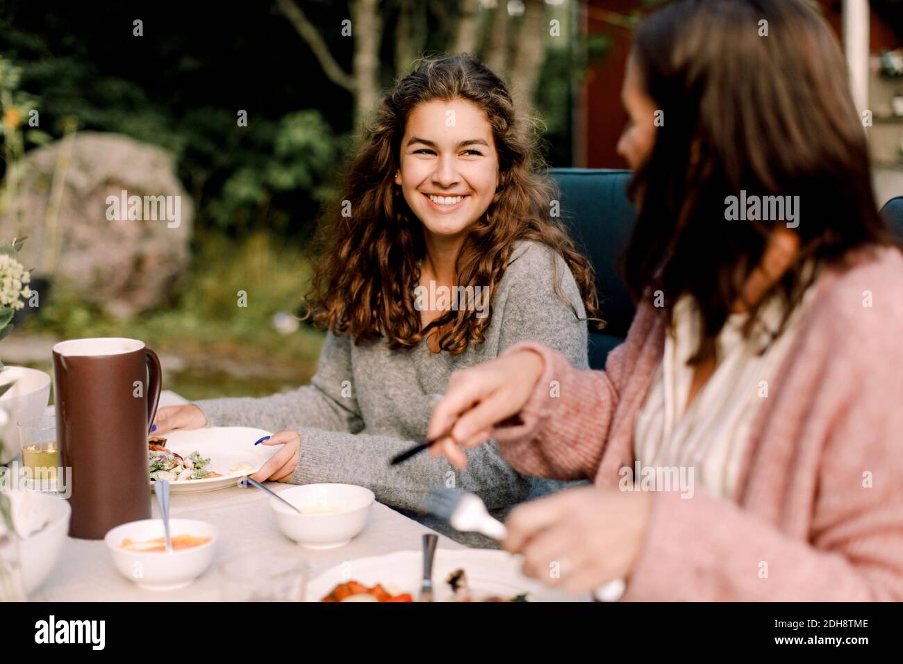 Donna sorridente che parla con la figlia mentre si siede al tavolo da pranzo in cortile Foto Stock