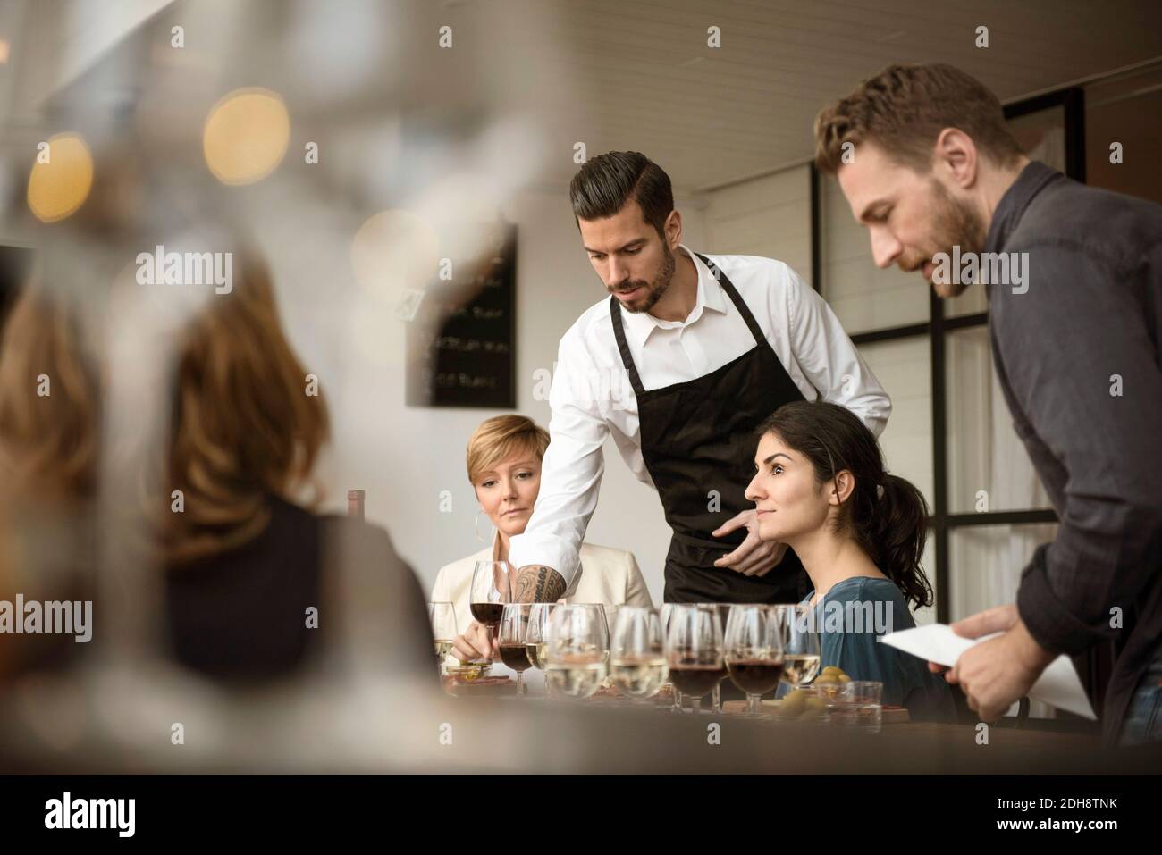 Uomo in grembiule disponendo vari wineglasses sul tavolo per affari persone Foto Stock