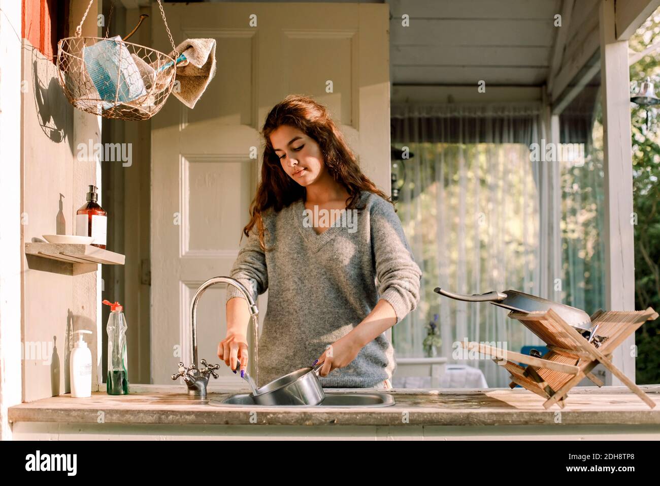 Adolescente ragazza lavaggio utensil in lavello fuori casa Foto Stock