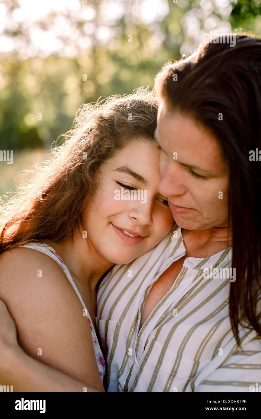 Madre sorridente che parla con la figlia mentre si abbraccia in cortile Foto Stock