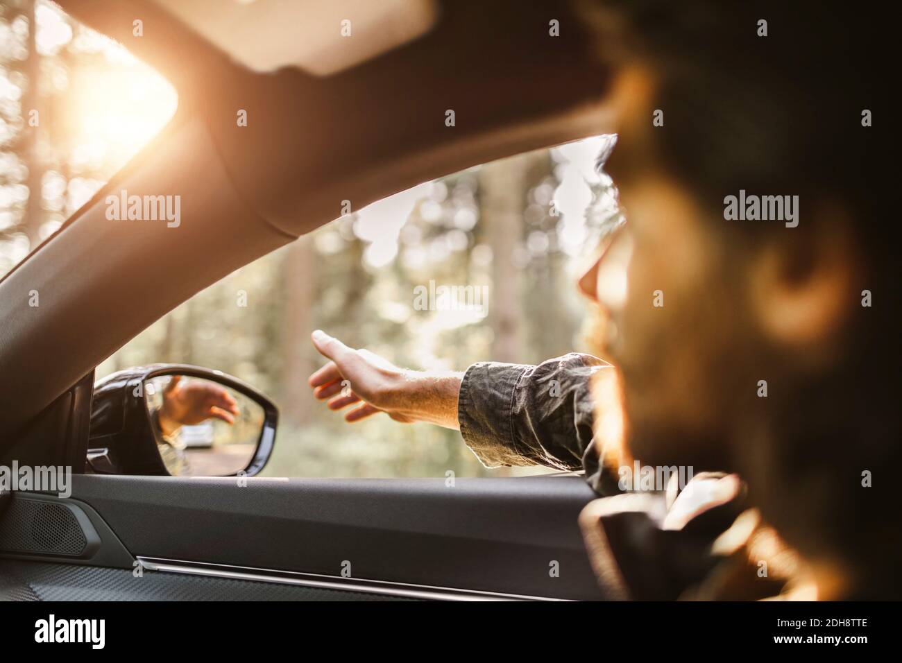 Giovane uomo con mano fuori dal finestrino dell'auto guardando via durante viaggio su strada Foto Stock