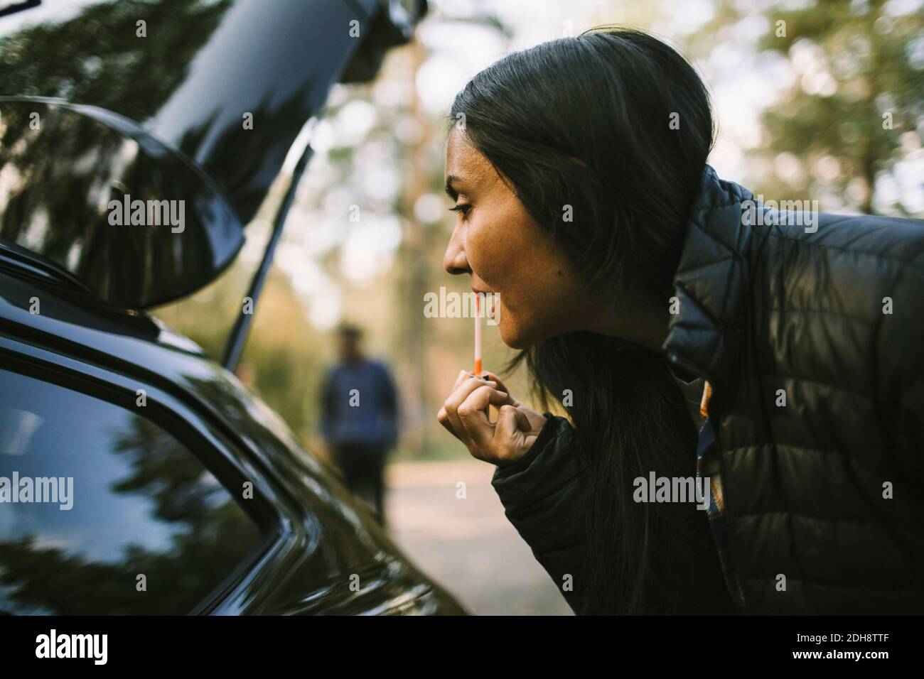 Vista laterale della donna che applica il rossetto mentre si guarda in auto finestra Foto Stock