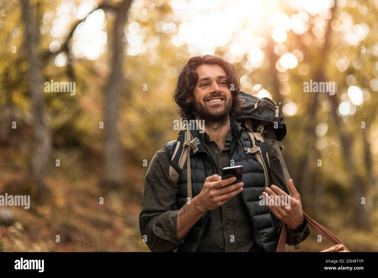 Sorridere con lo smartphone mentre si guarda lontano nella foresta Foto Stock