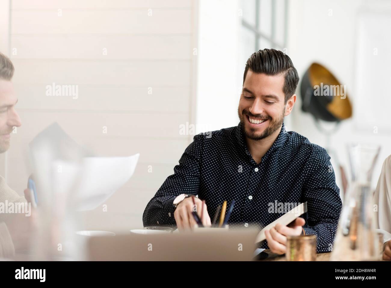Felice uomo d'affari che legge il documento mentre si siede al tavolo in ufficio Foto Stock