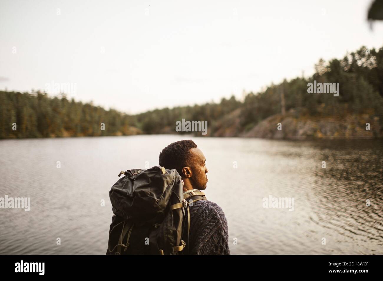 Vista posteriore dell'uomo con zaino che guarda lontano contro il lago in foresta Foto Stock
