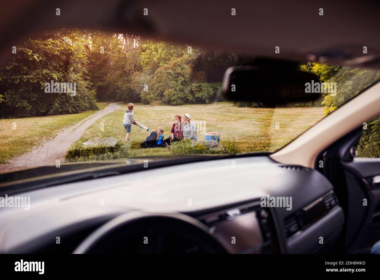 Famiglia sull'erba al parcheggio visto dal parabrezza dell'auto Foto Stock