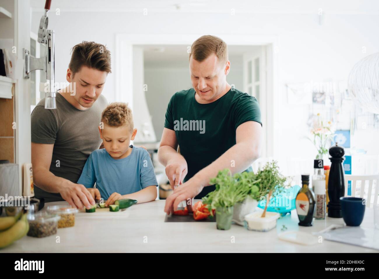 Padri omosessuali e figlio che tagliano cetriolo in cucina Foto Stock