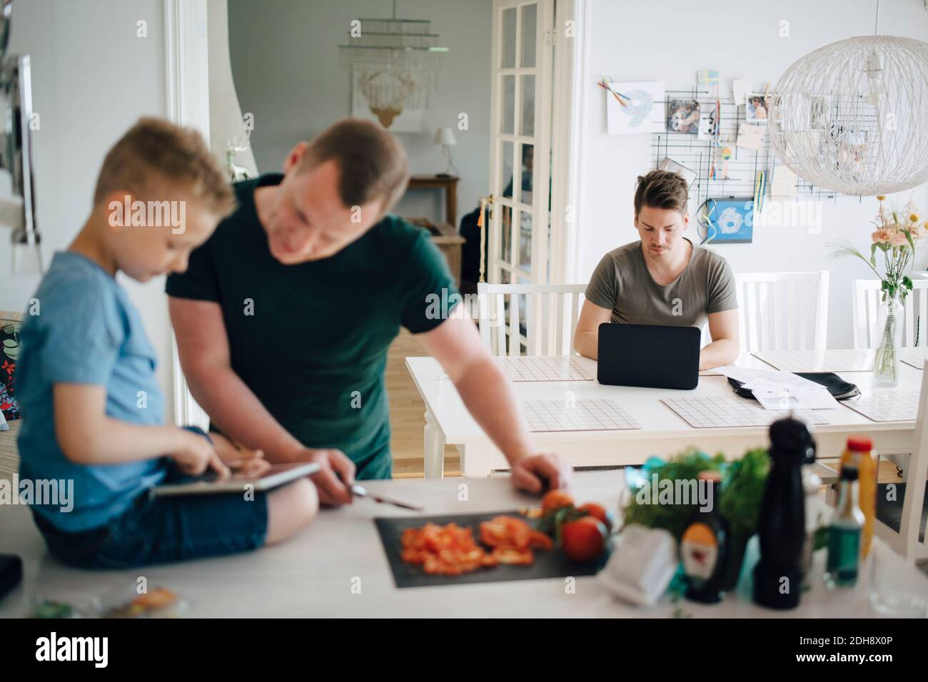 Uomo che usa un tavolo da pranzo portatile mentre padre e figlio cercano al tablet digitale sul bancone della cucina Foto Stock