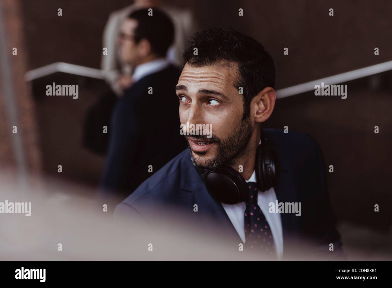 Uomo d'affari con cuffie che guardano lontano in città Foto Stock