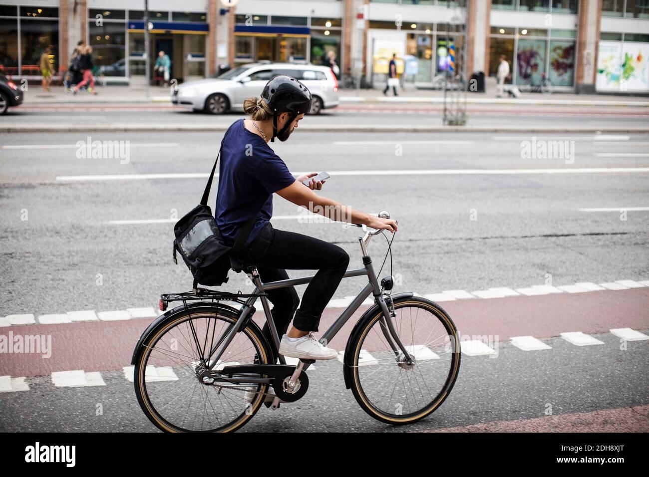 Uomo a tutta lunghezza che usa il telefono mentre si pedalano in città via Foto Stock