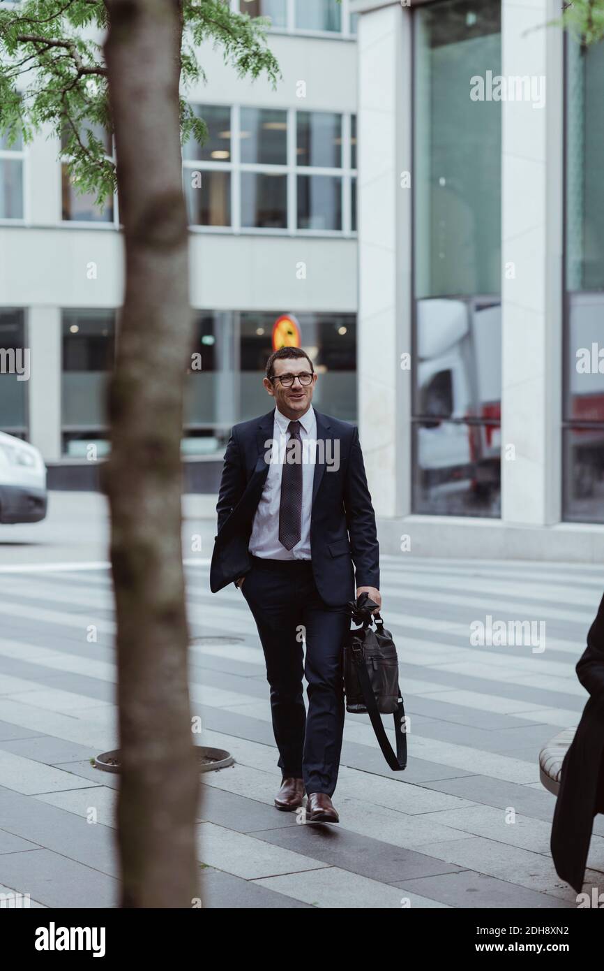 Sorridente imprenditore maschile con borsa a piedi in città Foto Stock