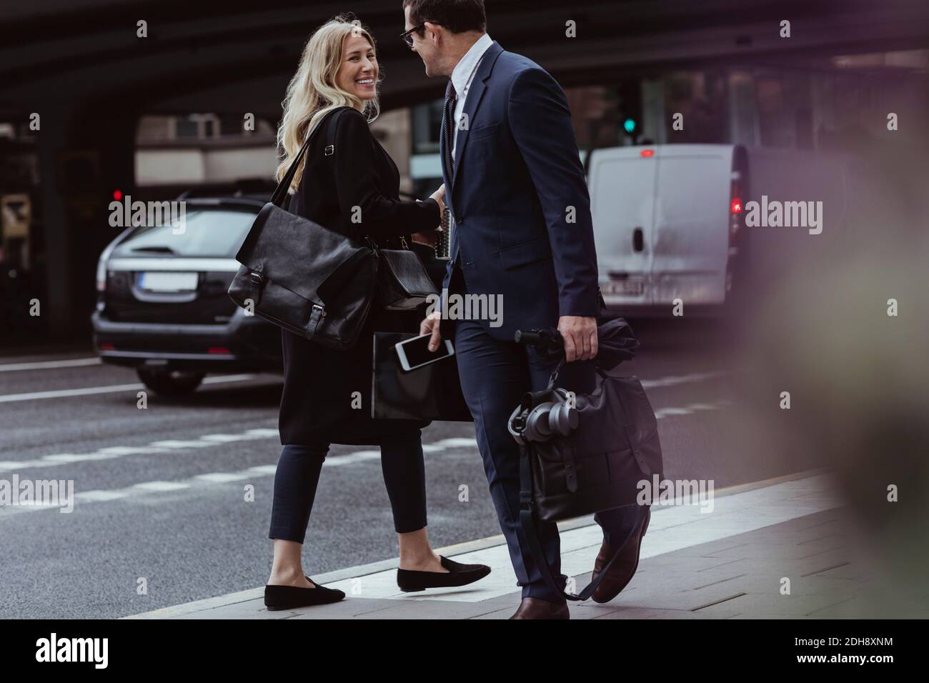 Uomo d'affari con borsa che parla con un collega sorridente mentre si cammina città Foto Stock