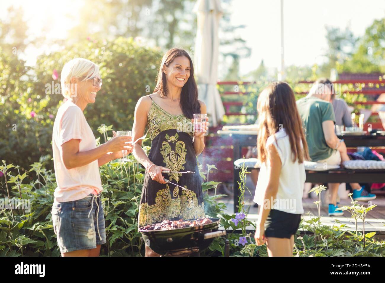 Donne felici che preparano il cibo sul barbecue mentre si guarda la ragazza nel cortile posteriore Foto Stock