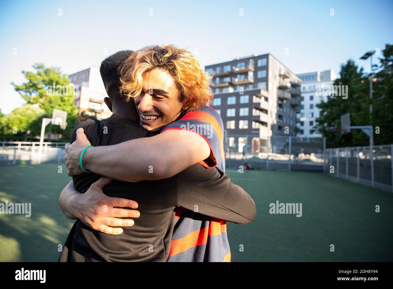 Amici felici si abbracciano mentre giocano in campo sportivo Foto Stock