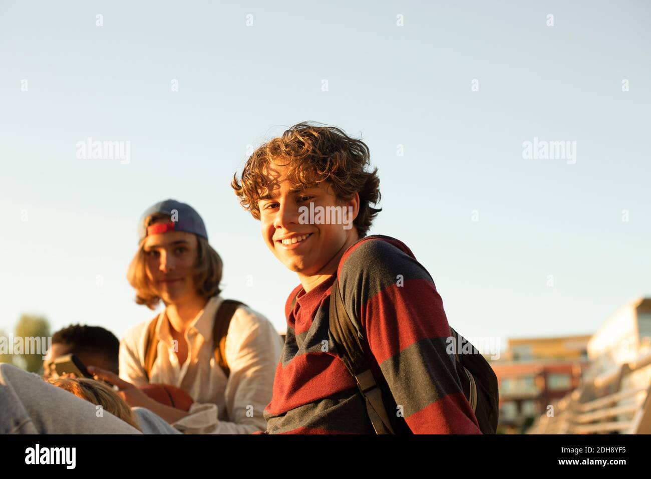 Ritratto di sorridente adolescente maschile con gli amici che si divertono contro chiaro cielo Foto Stock