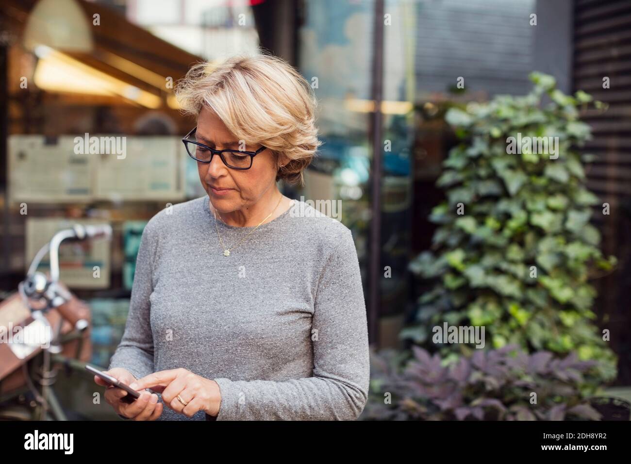 Donna d'affari matura che usa lo smartphone al bar del marciapiede Foto Stock