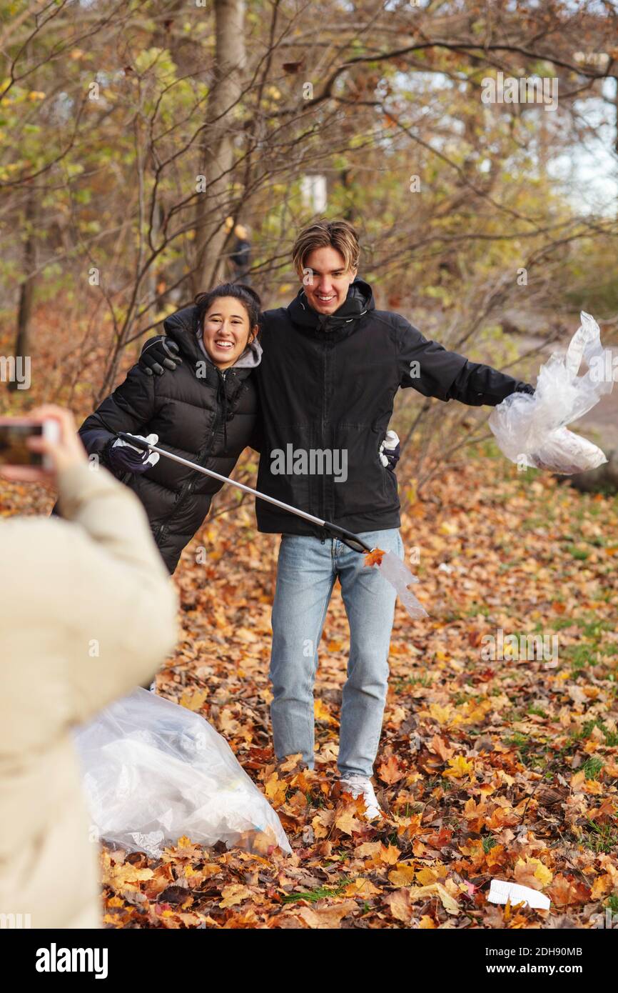 Giovane ambientalista che fotografa amici sorridenti che tengono in parco le microplastiche Foto Stock