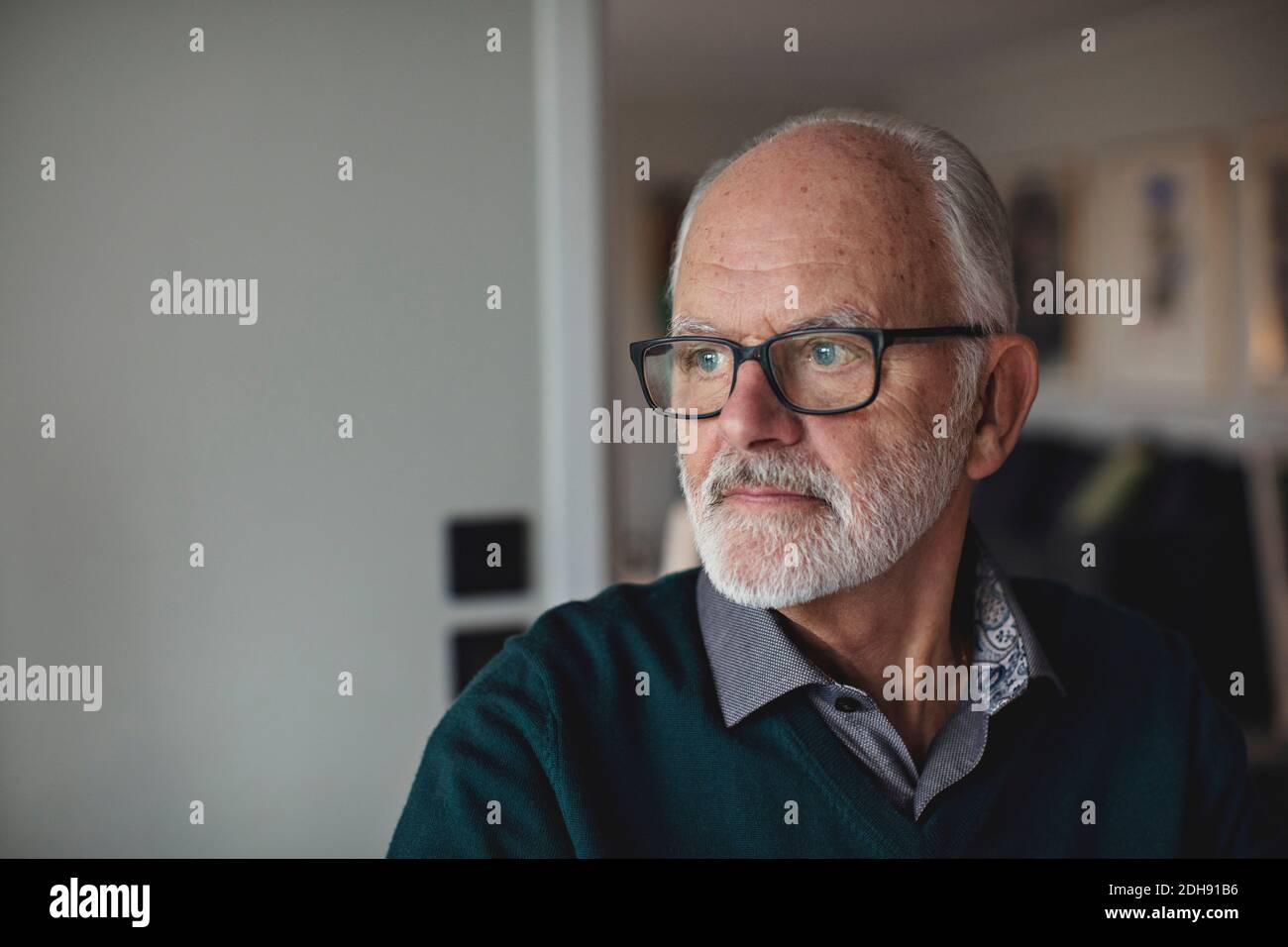 Contemplare l'uomo anziano che indossa gli occhiali mentre si guarda via a casa Foto Stock