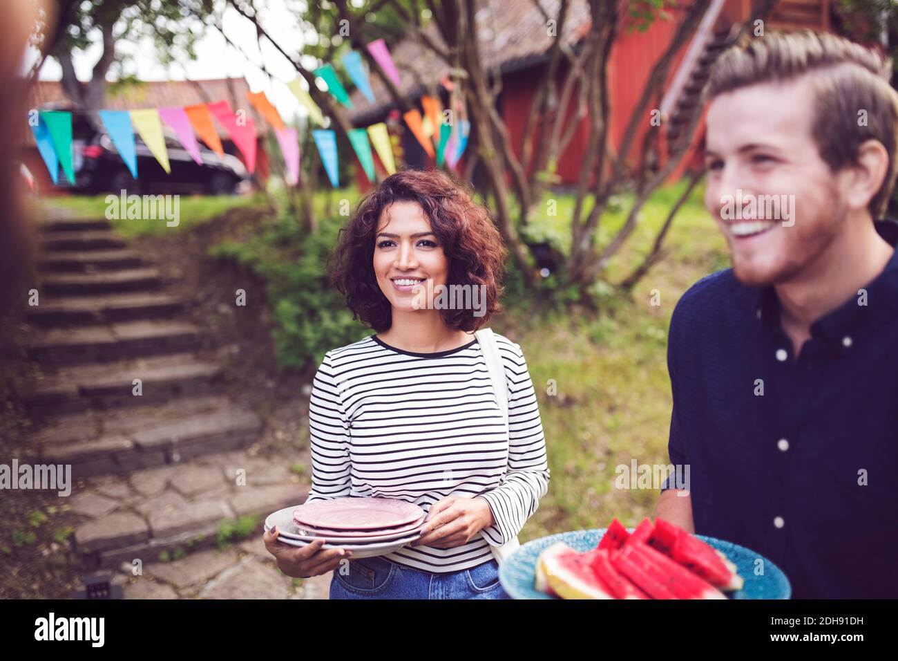 Sorridendo gli amici che tengono le piastre mentre si levano in piedi nel cortile posteriore durante festa in giardino Foto Stock