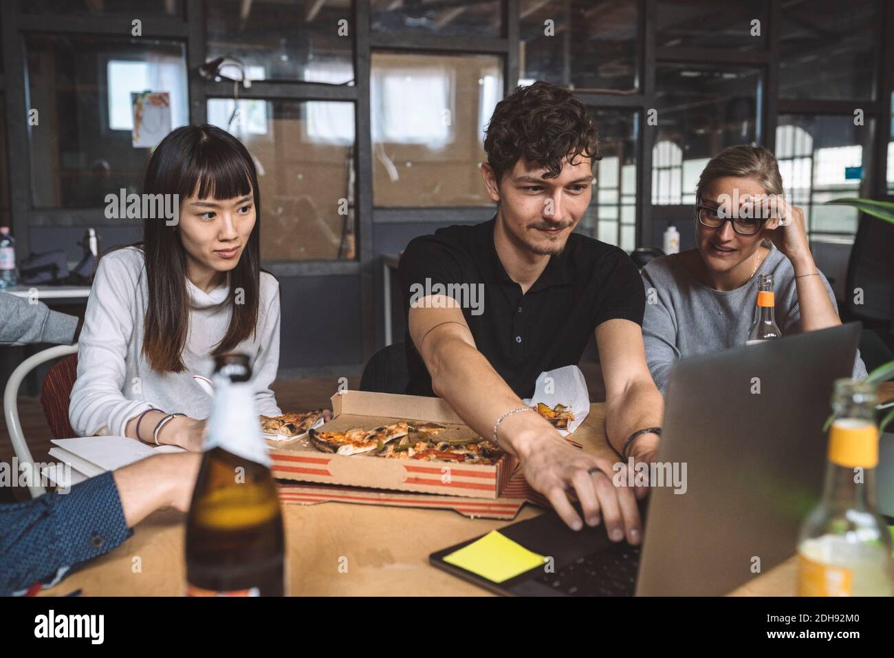 Sorridendo i colleghi con la pizza che lavora sul posto di lavoro Foto Stock