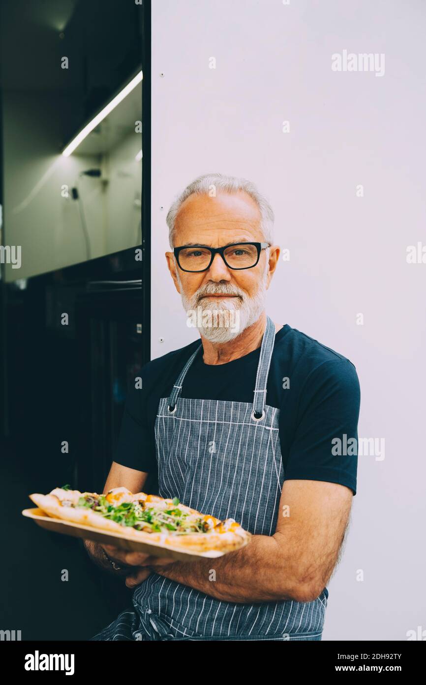 Fidato proprietario senior con piatto alimentare in piedi contro terra commerciale veicolo Foto Stock