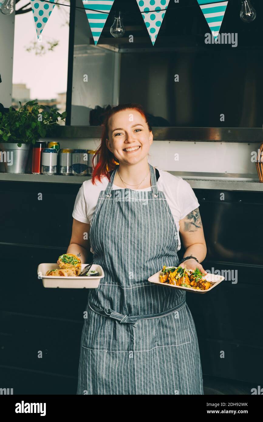 Ritratto di sorridente proprietario che tiene piatto di cibo indiano contro commerciale veicolo terrestre Foto Stock