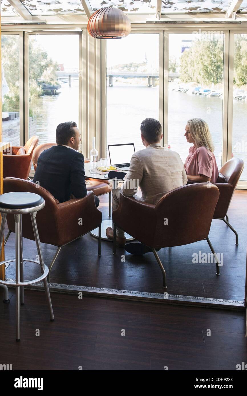 Colleghi di lavoro seduti con un computer portatile durante la riunione al ristorante Foto Stock