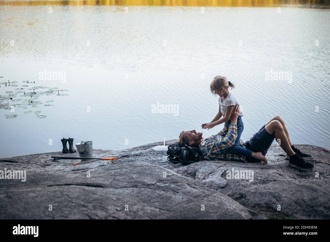Vista laterale della figlia seduta sul padre sorridente al lago Foto Stock