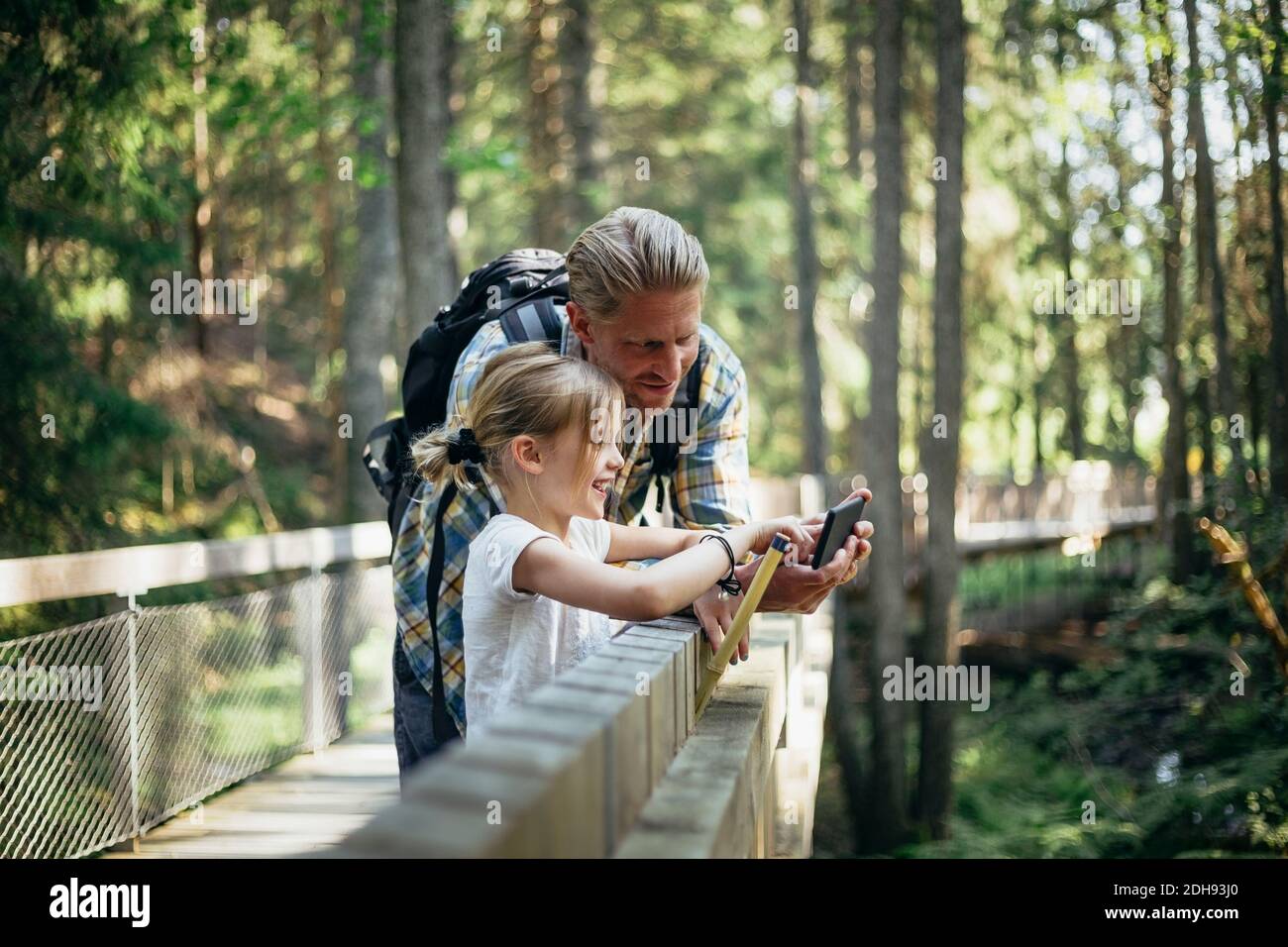 Sorridente padre con zaino e figlia che guarda lo smartphone in foresta Foto Stock
