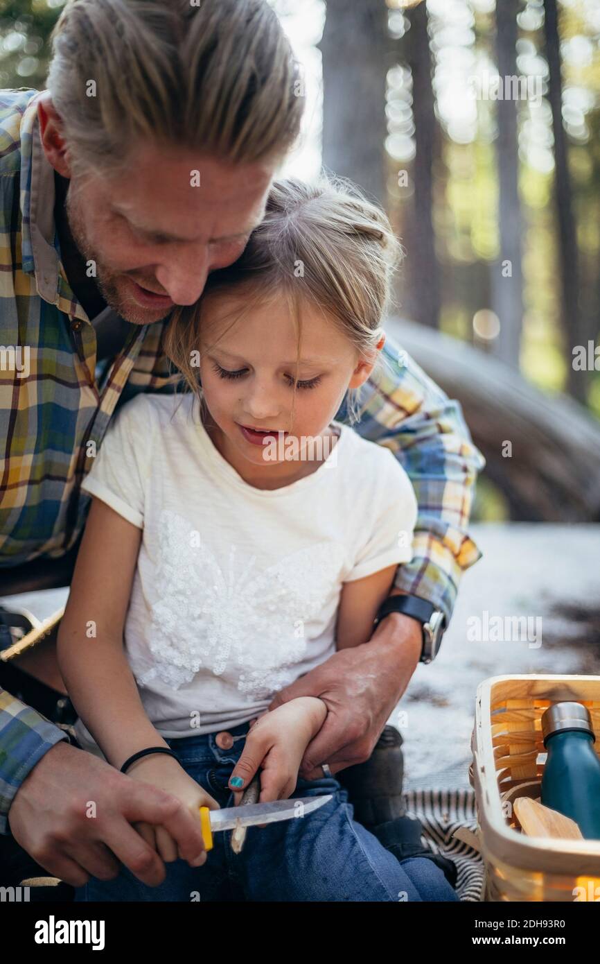 Padre che aiuta la figlia nel taglio bastone nella foresta Foto Stock
