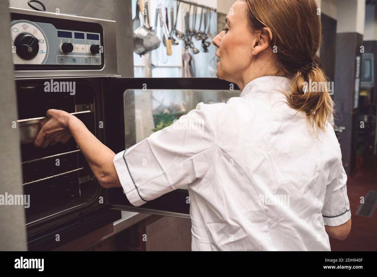 Vista posteriore dello chef che mette la teglia in forno Foto Stock