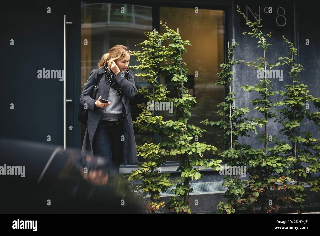 Uomo d'affari medio adulto che usa il dispositivo a mani libere mentre attraversa la strada Foto Stock