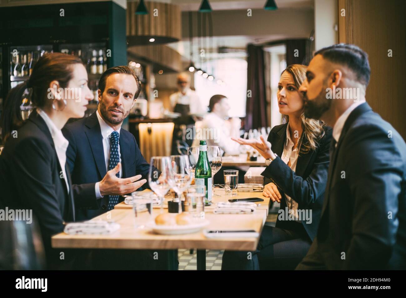 Professionisti di sesso maschile e femminile che parlano mentre sono seduti per un pranzo di lavoro nel ristorante Foto Stock