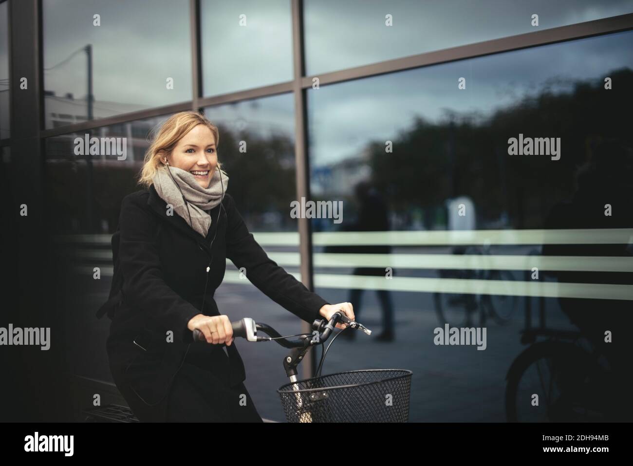 Sorridente donna d'affari di media età che corre in bicicletta vicino all'edificio della città Foto Stock