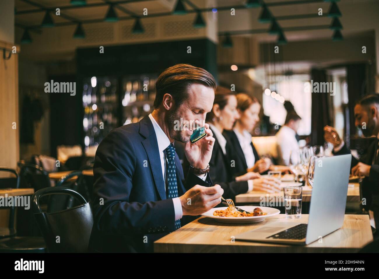 Sorridente uomo d'affari che parla al telefono mentre mangia cibo nel ristorante Foto Stock