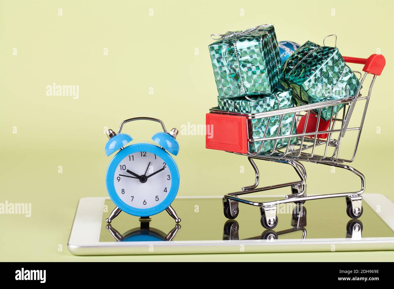 Online, shopping natalizio. Carrello supermercato con scatole regalo, tablet pc e orologio su sfondo verde. Spazio per la copia Foto Stock