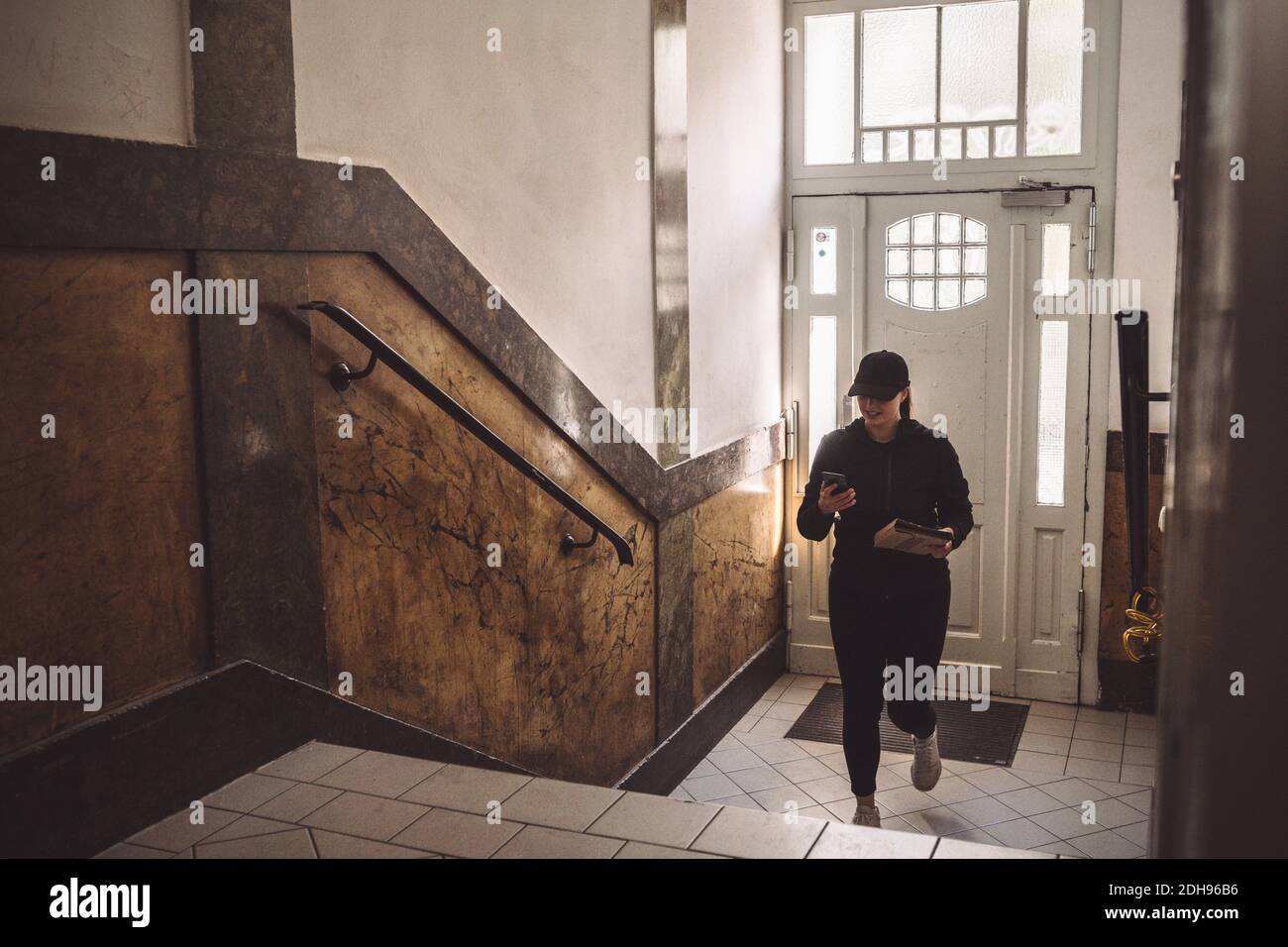 Consegna donna con pacchetto che guarda il telefono mentre salendo scale Foto Stock