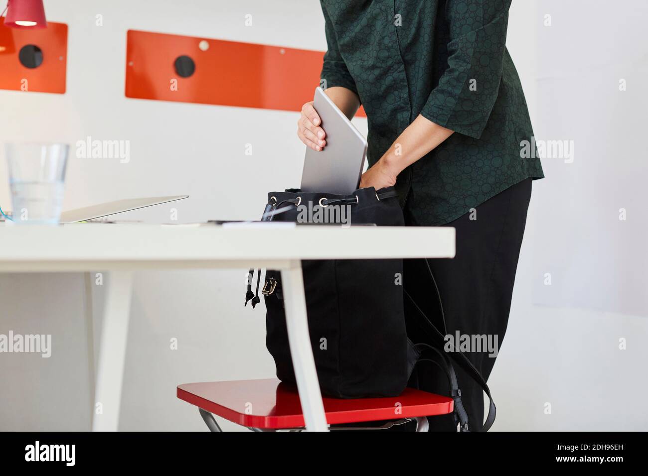 Metà della donna d'affari che tiene il portatile in borsa in ufficio Foto Stock