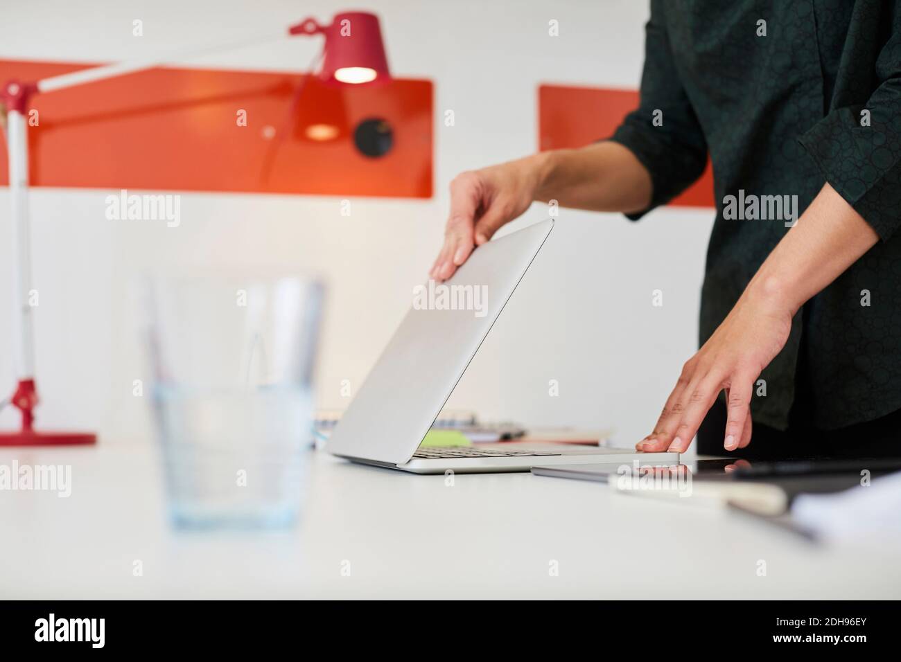 Sezione centrale di businesswoman adulto medio che apre il laptop al tavolo dentro ufficio Foto Stock